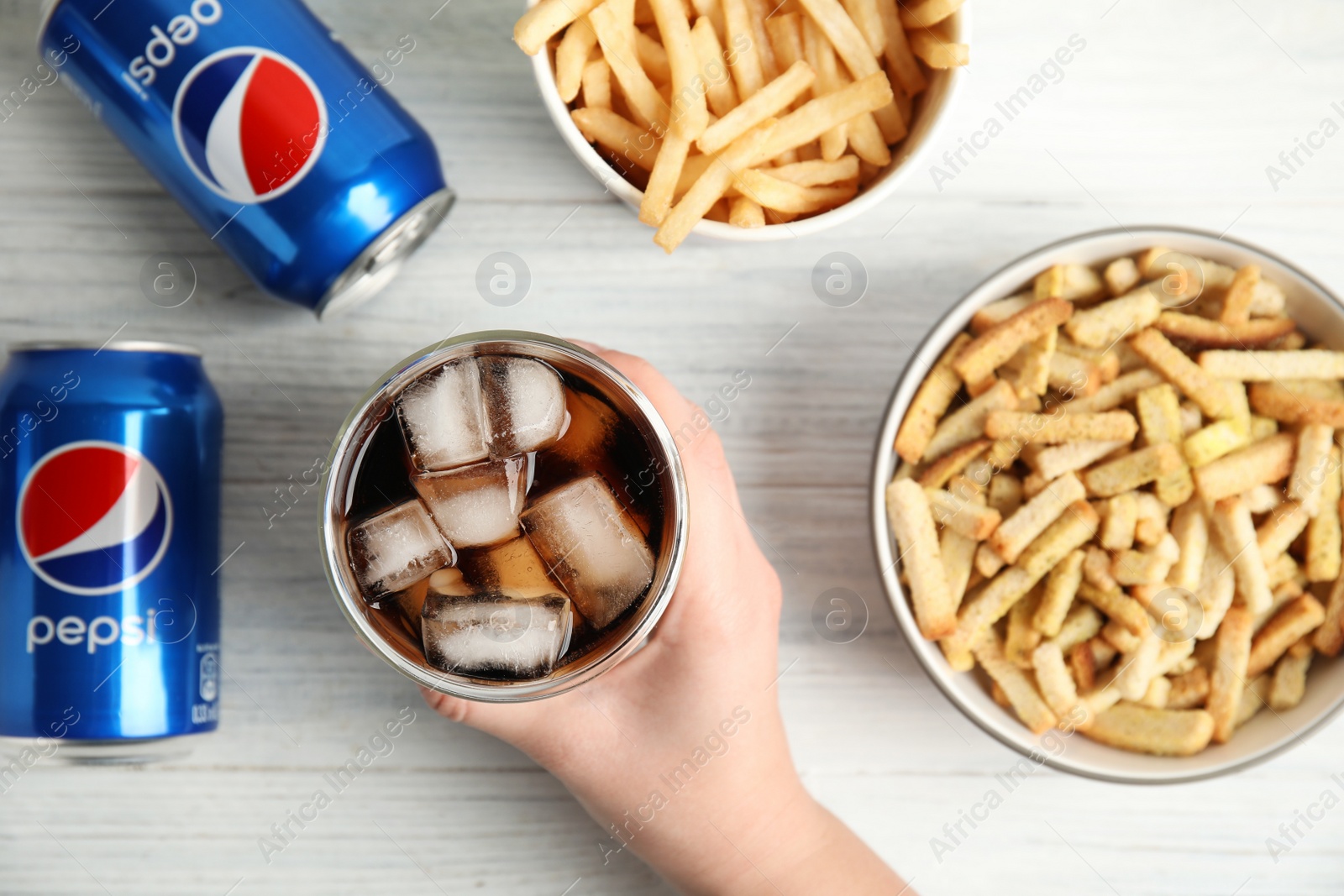 Photo of MYKOLAIV, UKRAINE - FEBRUARY 15, 2021: Woman with glass of Pepsi at white wooden table, top view