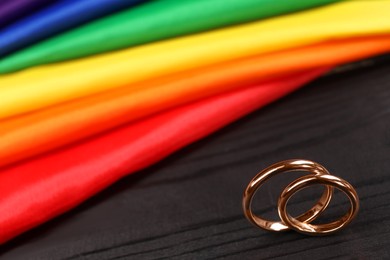 Photo of Rainbow LGBT flag and wedding rings on black wooden background, closeup