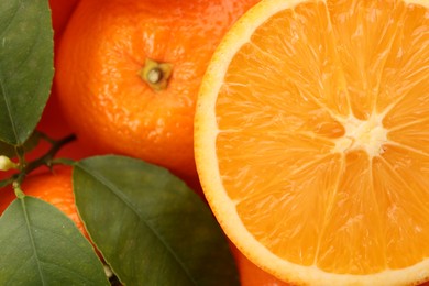 Photo of Cut and whole fresh ripe oranges with green leaves as background, top view