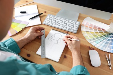 Man drawing in sketchbook with pencil and ruler at wooden table, closeup