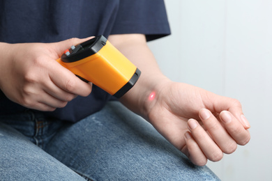 Woman measuring temperature with non contact infrared thermometer on light background, closeup