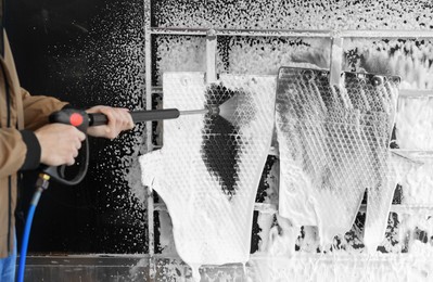 Photo of Man cleaning auto mats with high pressure water jet at self-service car wash, closeup