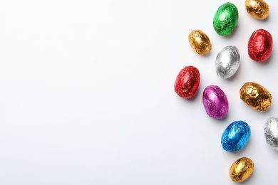 Chocolate eggs wrapped in colorful foil on white background, flat lay. Space for text