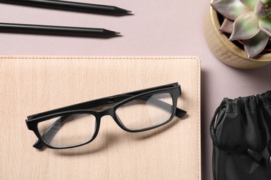 Stylish pair of glasses, pencils, succulent and notebook on light grey table, flat lay