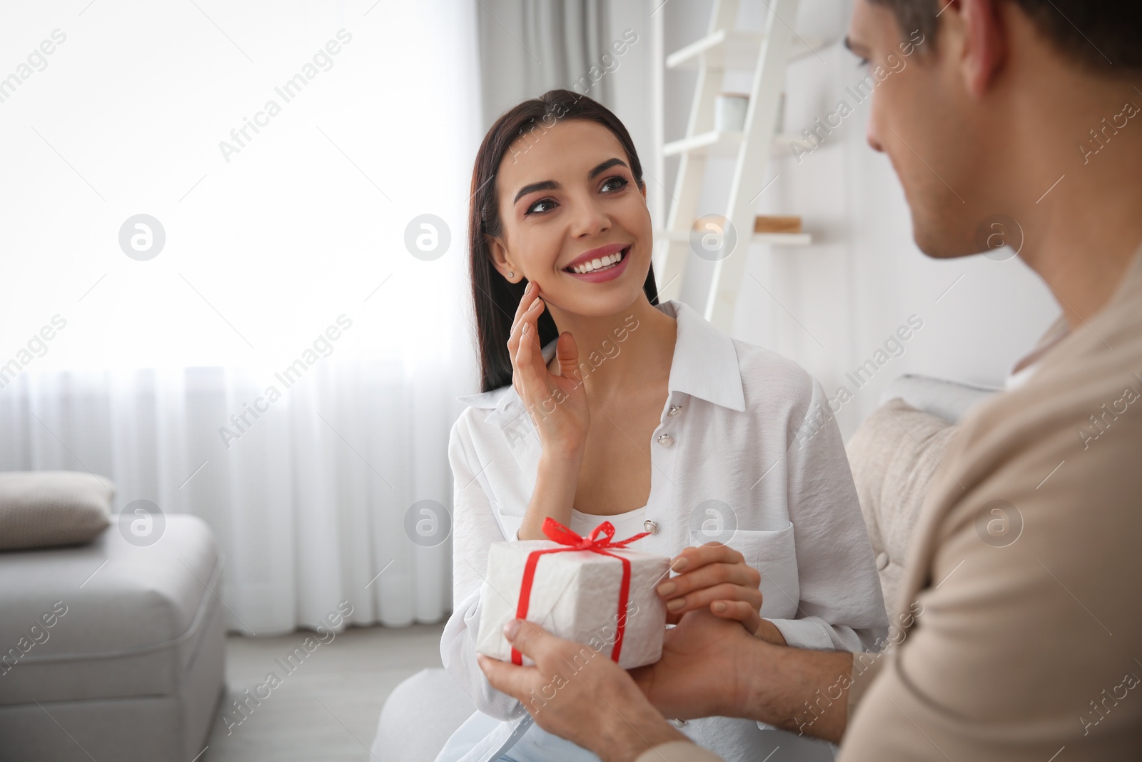 Photo of Man presenting gift to his beloved woman at home. Valentine's day celebration