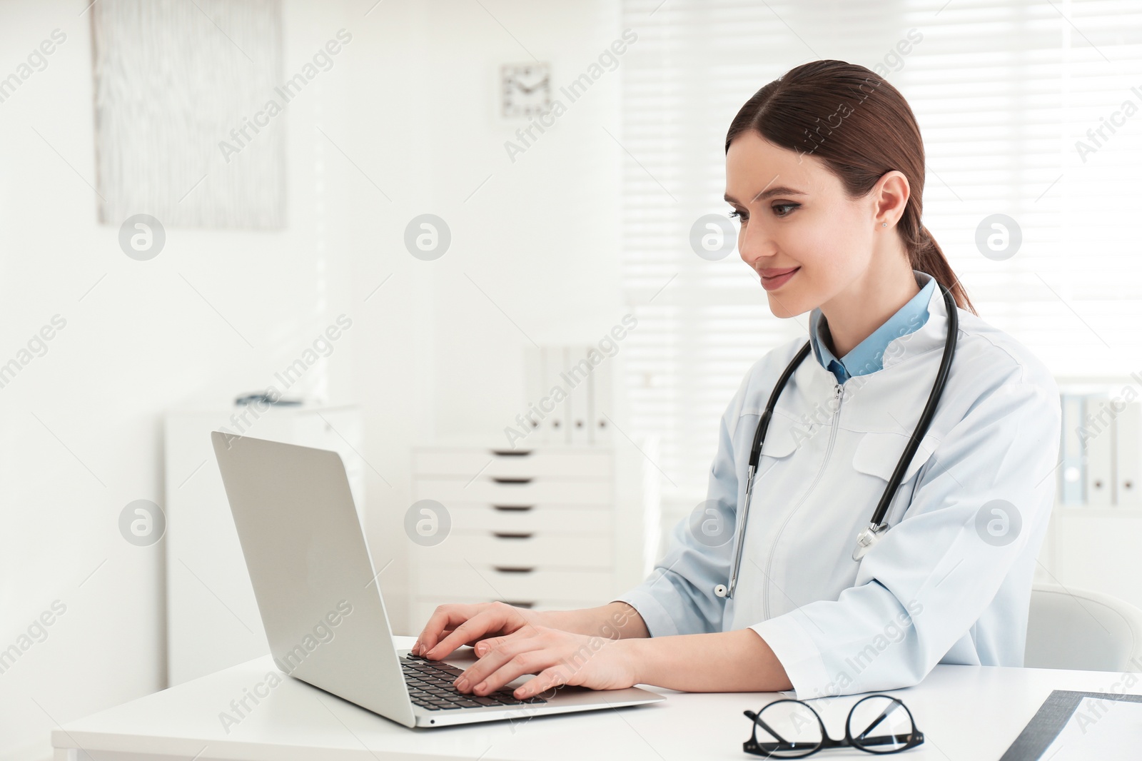 Photo of Young female doctor working with laptop at table in office