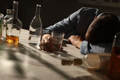 Photo of Addicted man with alcoholic drink sleeping at table indoors