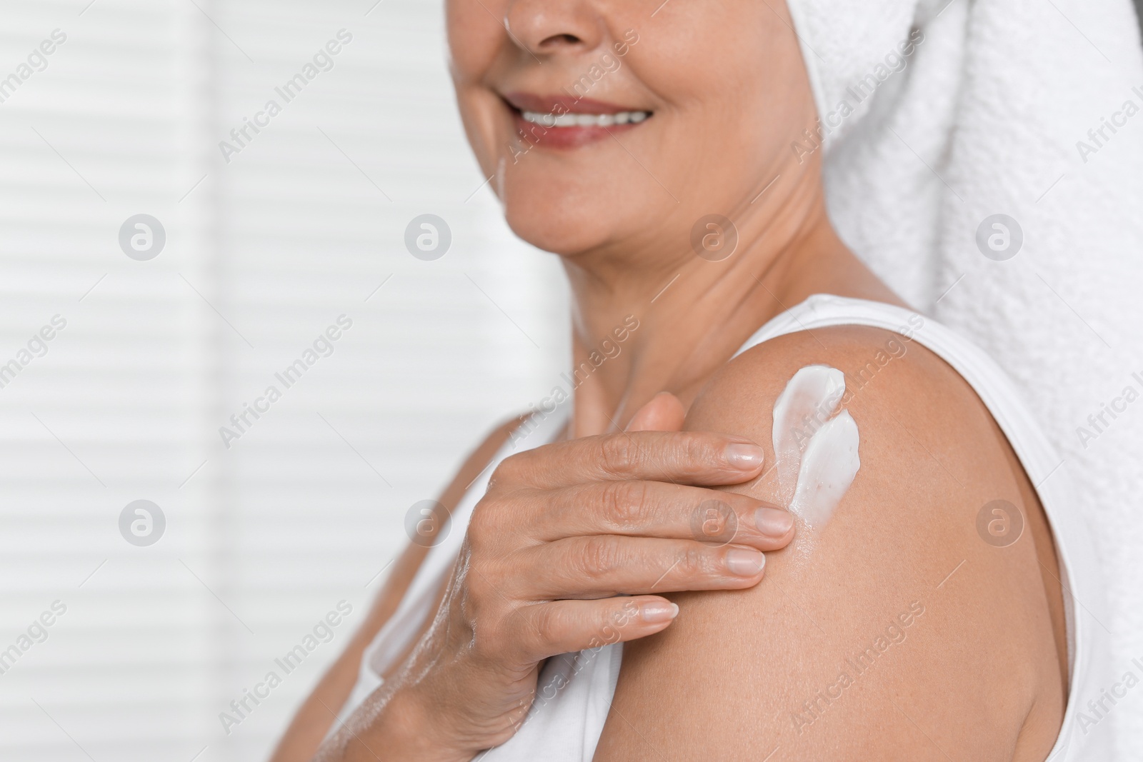 Photo of Happy woman applying body cream onto shoulder indoors, closeup. Space for text