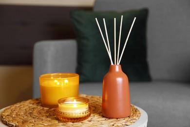 Photo of Aromatic reed air freshener and scented candles on table indoors