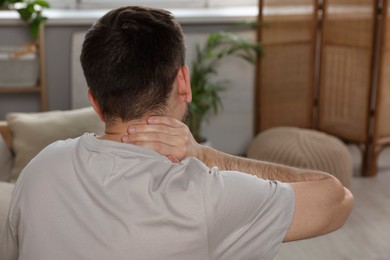 Man suffering from neck pain in living room, back view