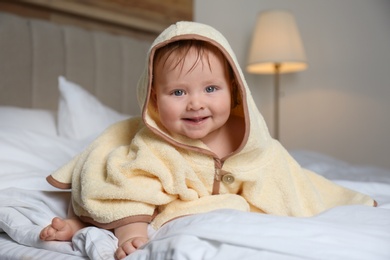 Photo of Cute little baby in yellow hooded towel on bed after bath