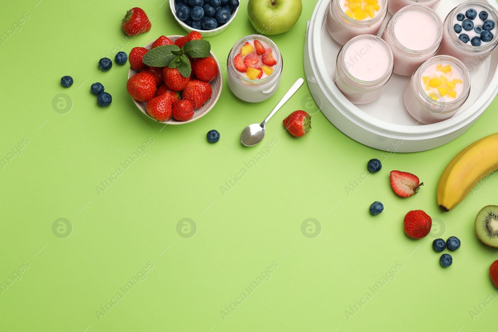 Photo of Yogurt maker with jars and different fruits on light green background, flat lay. Space for text