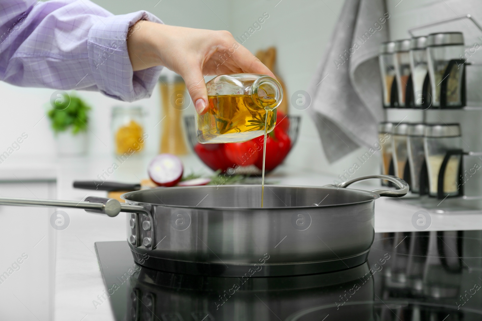 Photo of Woman pouring aromatic cooking oil from bottle into frying pan in kitchen, closeup