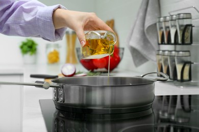 Woman pouring aromatic cooking oil from bottle into frying pan in kitchen, closeup