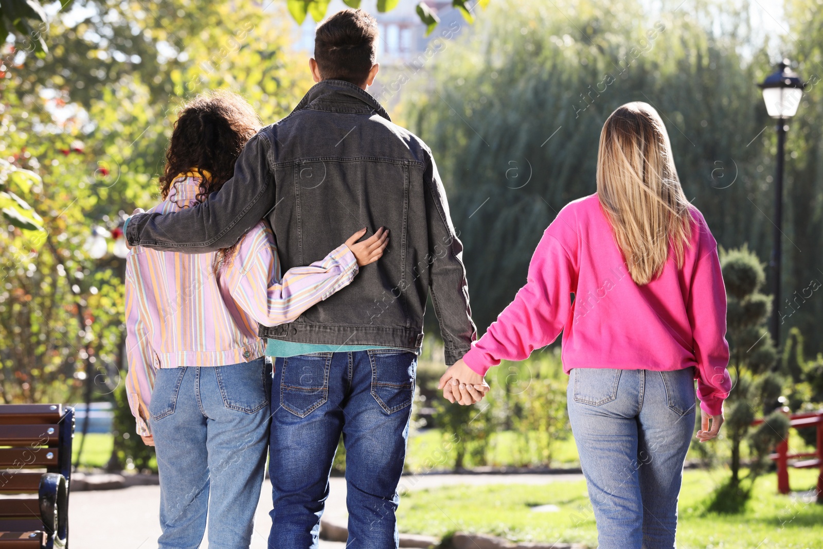 Photo of Man holding hands with another woman while hugging his girlfriend during walk in park, back view. Love triangle