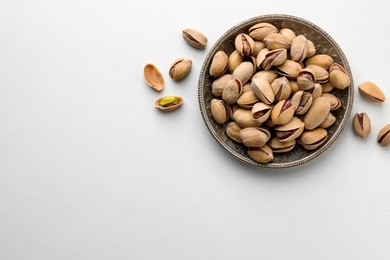 Plate and pistachio nuts on white background, flat lay. Space for text