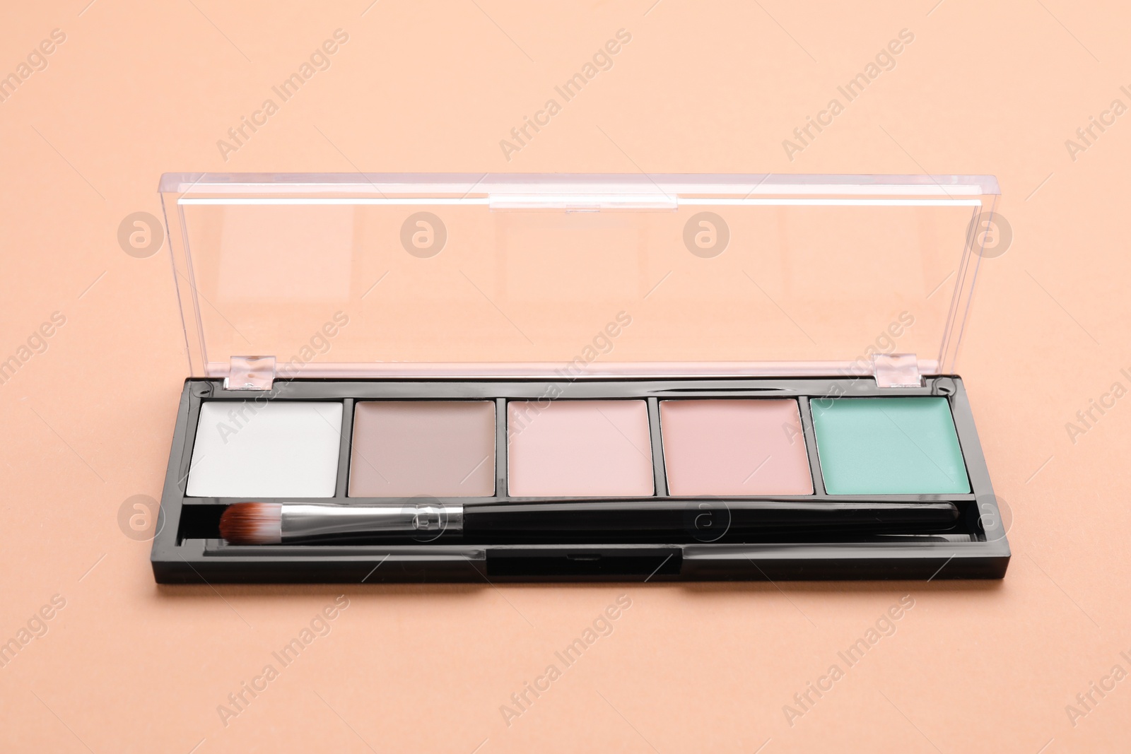 Photo of Colorful contouring palette with brush on beige background, closeup. Professional cosmetic product