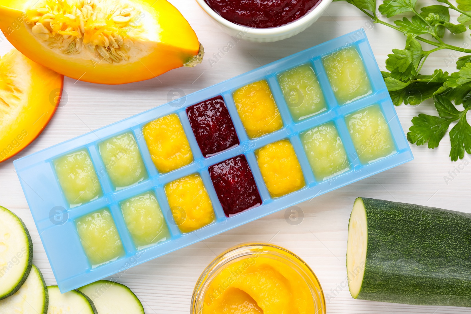 Photo of Different purees in ice cube tray and ingredients on white table, flat lay. Ready for freezing