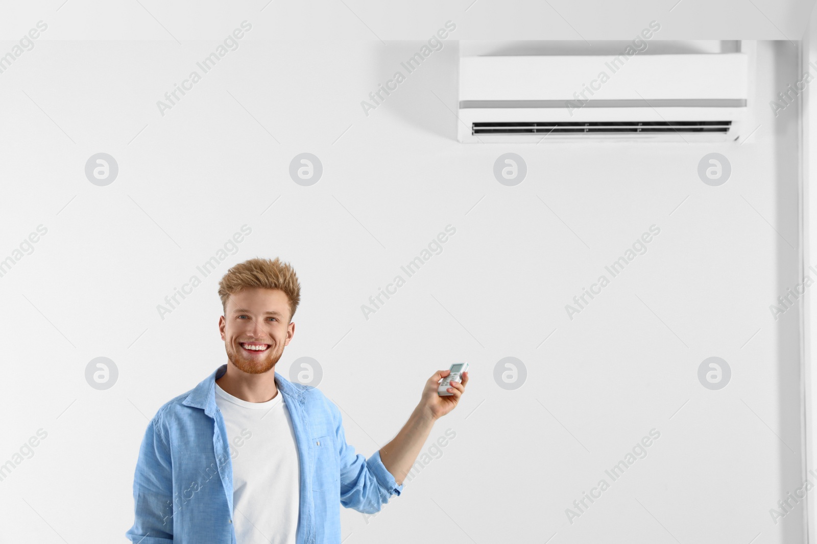 Photo of Young man operating air conditioner with remote control indoors. Space for text