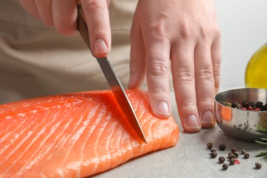 Photo of Man cutting raw salmon at grey table, closeup