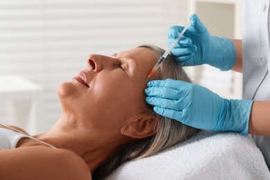 Doctor giving facial injection to senior woman in clinic, closeup. Cosmetic surgery