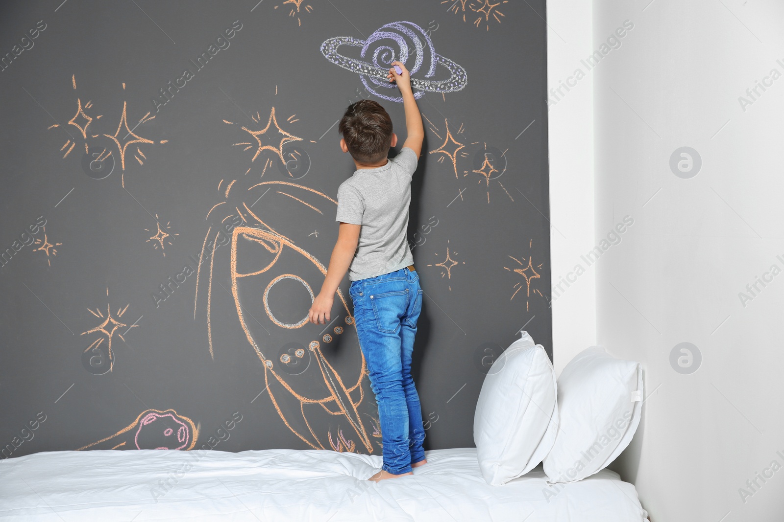 Photo of Little child drawing rocket with chalk on wall in bedroom