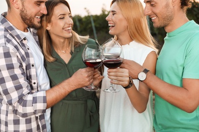 Friends holding glasses of wine and having fun on vineyard picnic