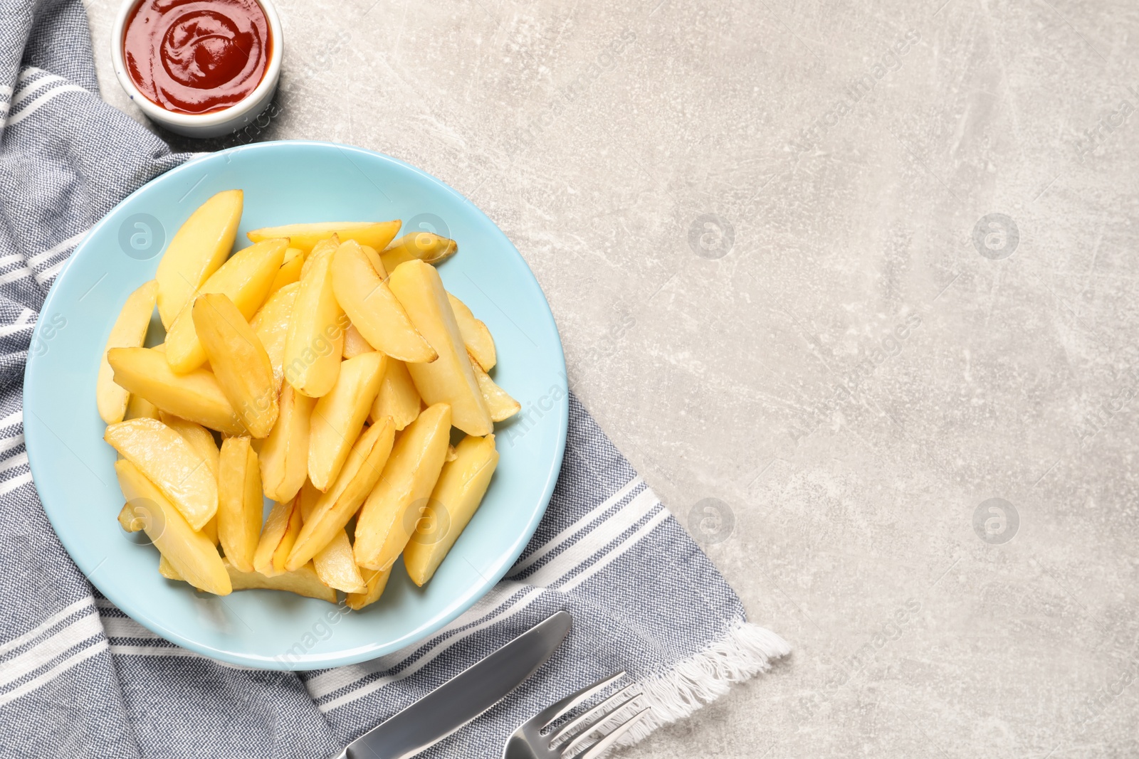 Photo of Plate with tasty baked potato wedges and sauce on grey table, flat lay. Space for text