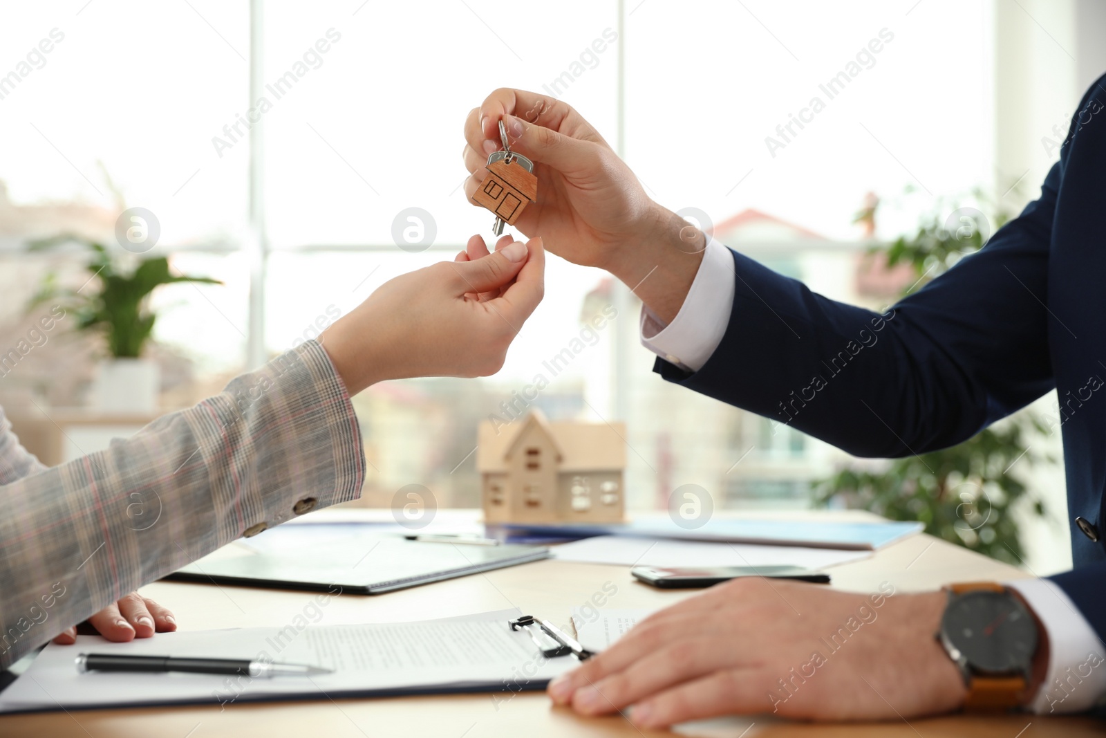 Photo of Real estate agent giving key with trinket to client in office, closeup