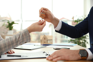 Photo of Real estate agent giving key with trinket to client in office, closeup