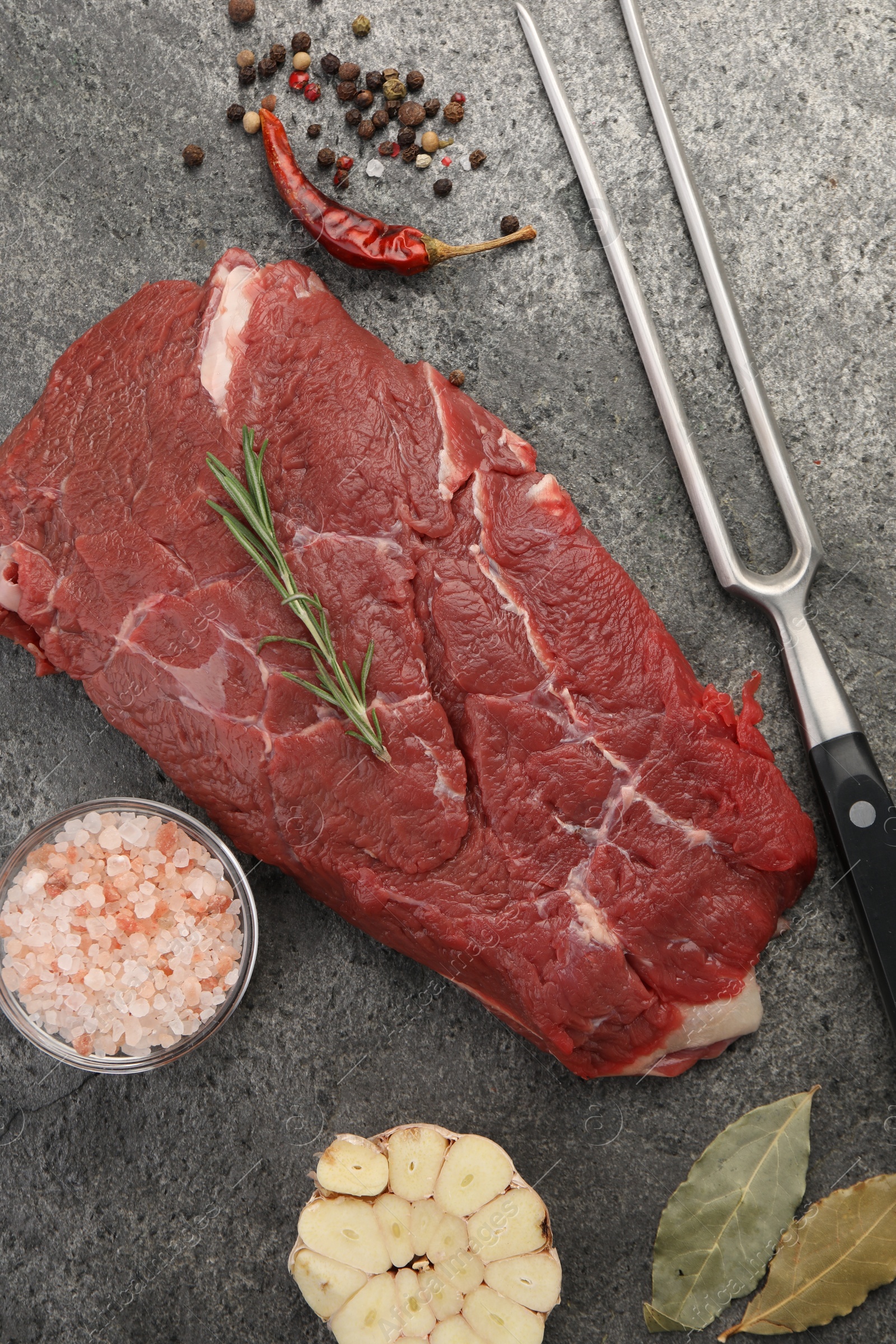 Photo of Piece of raw beef meat, spices, rosemary and fork on grey table, flat lay