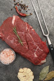 Piece of raw beef meat, spices, rosemary and fork on grey table, flat lay