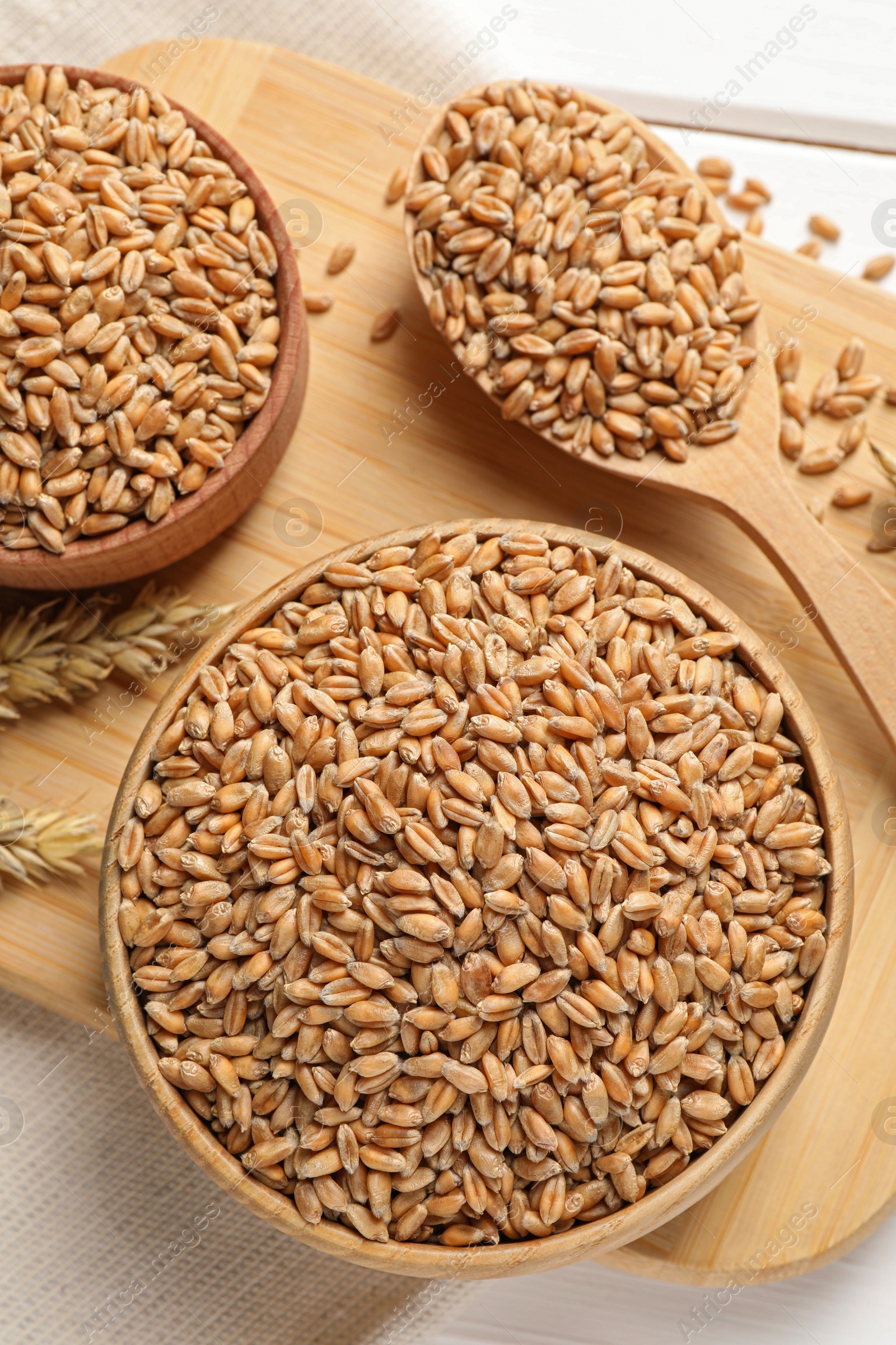 Photo of Wheat grains in bowls and spoon on wooden board, flat lay