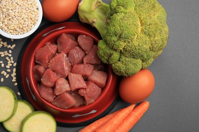 Raw meat in bowl and healthy products for pet on black background, flat lay