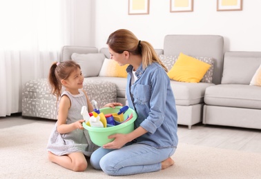 Photo of Housewife and daughter with basket full of detergents on carpet at home