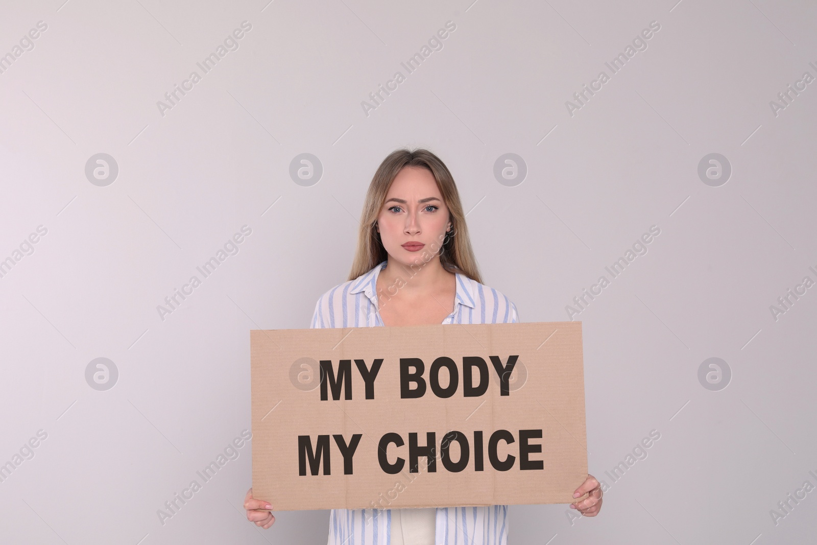 Image of Woman holding placard with phrase My Body My Choice on light grey background. Abortion protest