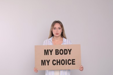 Image of Woman holding placard with phrase My Body My Choice on light grey background. Abortion protest
