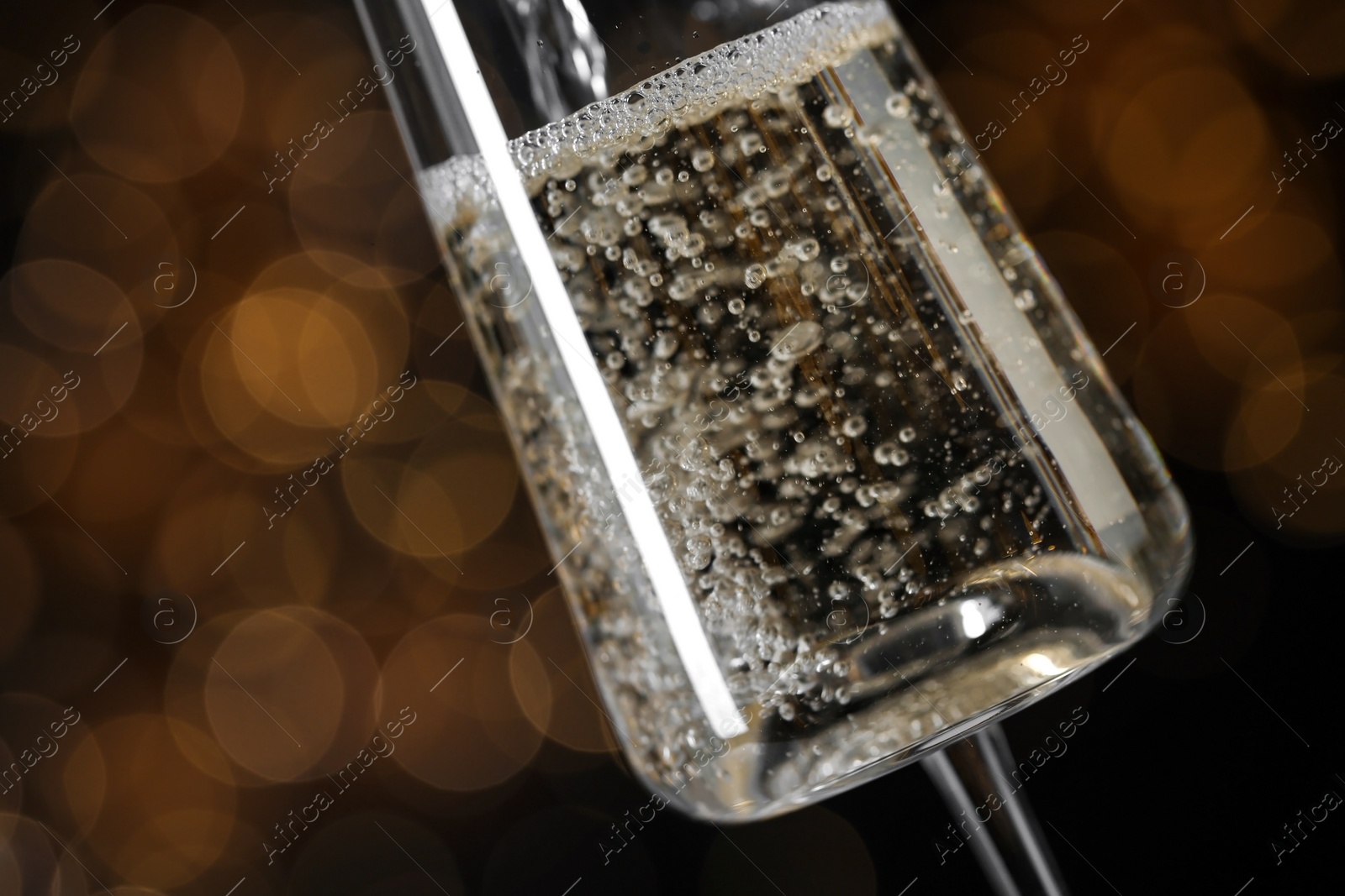 Photo of Pouring champagne into glass against blurred lights, closeup