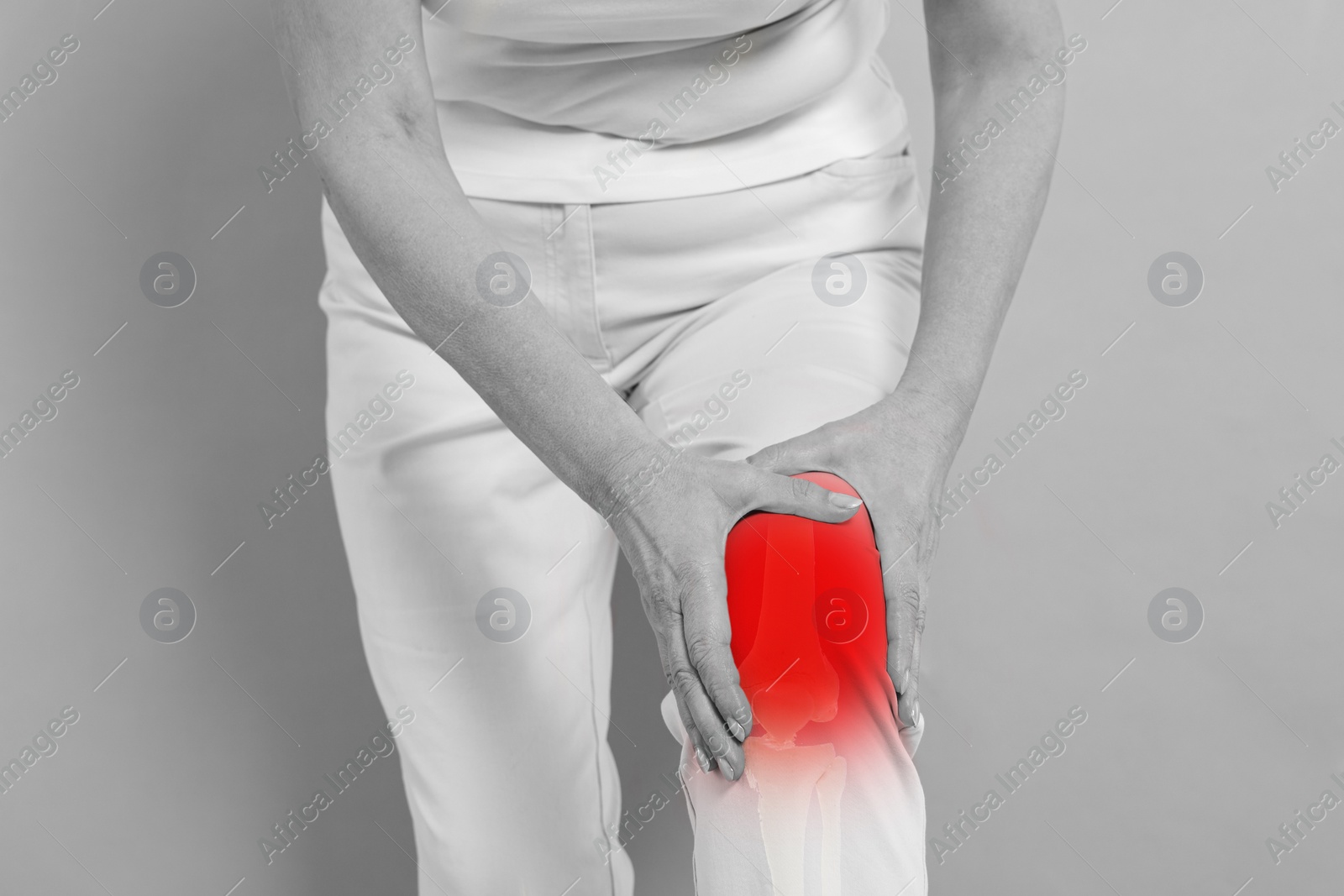 Image of Arthritis symptoms. Woman suffering from pain in her knee on background, closeup. Black and white effect with red accent in painful area