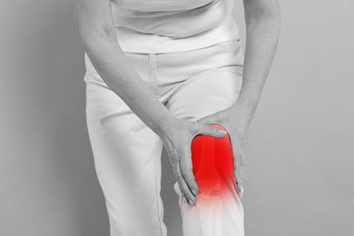 Arthritis symptoms. Woman suffering from pain in her knee on background, closeup. Black and white effect with red accent in painful area