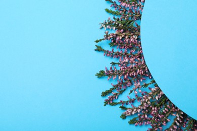 Heather branches with beautiful flowers and blank card on light blue background, flat lay. Space for text