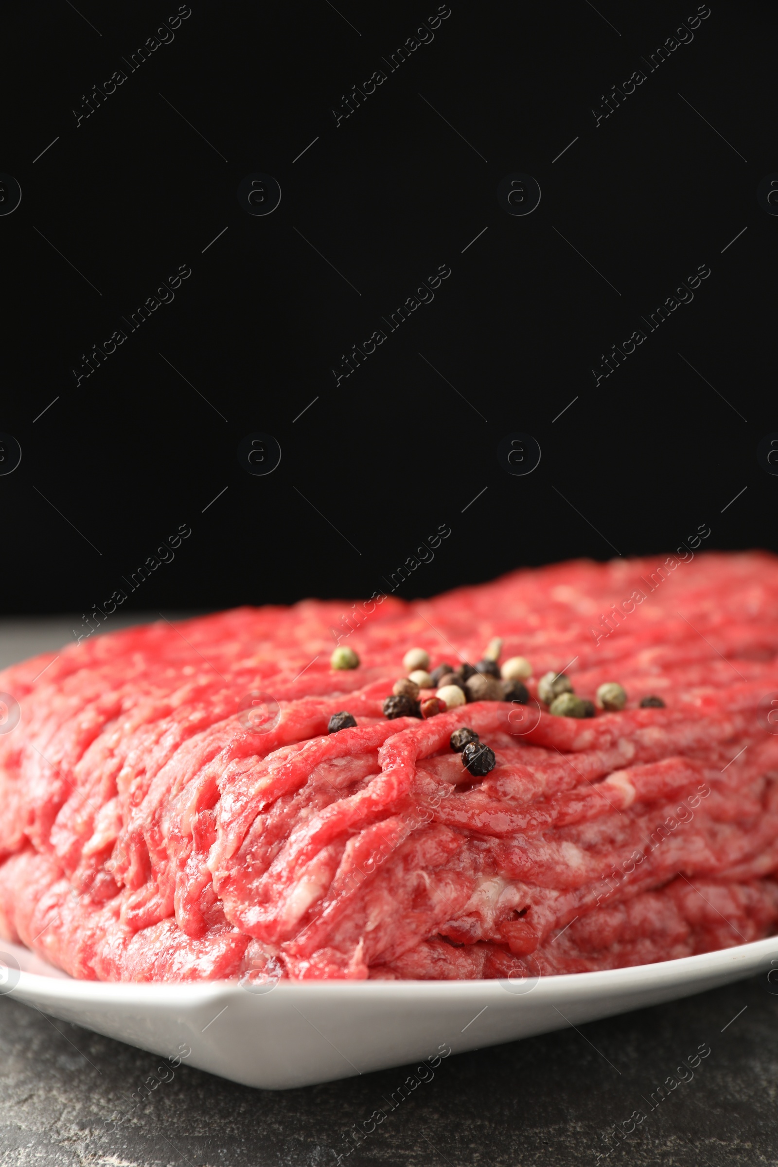 Photo of Raw ground meat and peppercorns on grey table, closeup