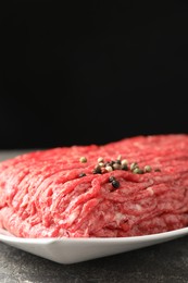 Photo of Raw ground meat and peppercorns on grey table, closeup