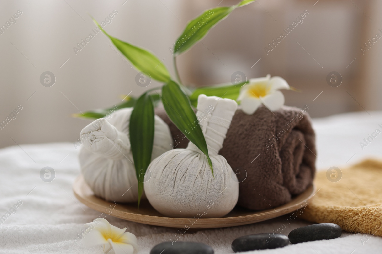 Photo of Spa stones, flowers and herbal bags on towel indoors, closeup