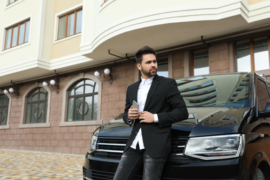 Photo of Handsome young man with smartphone near modern car outdoors