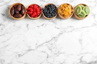 Bowls of different dried fruits on marble background, top view with space for text. Healthy lifestyle