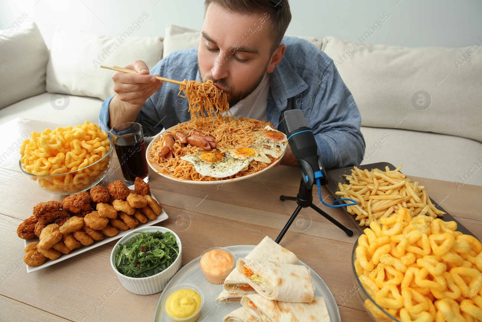 Photo of Food blogger eating in front of microphone at table. Mukbang vlog