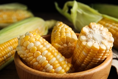 Photo of Tasty sweet corn cobs in bowl on table, closeup view