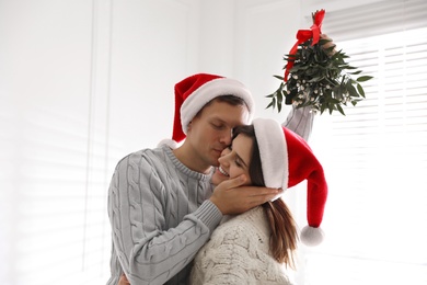 Happy man kissing his girlfriend under mistletoe bunch at home