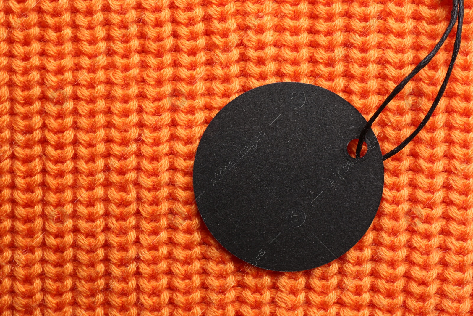 Photo of Circle shaped tag with space for text on orange knitted background, top view